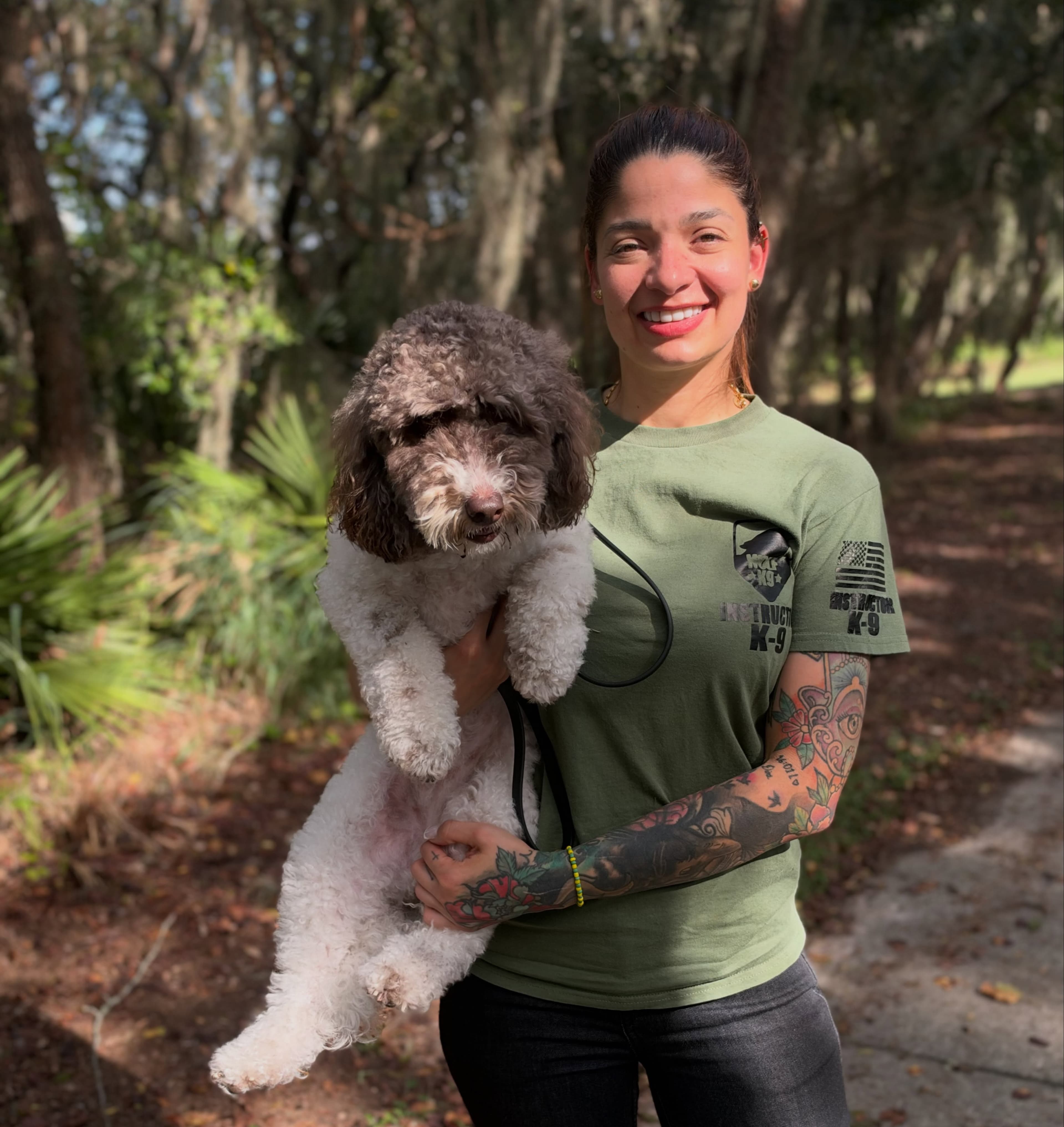 Trainer hugging Cookie, a goldendoodle, under the trees